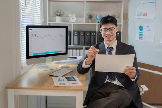 Asian Businessman or Stock Trader Analyzing Financial Market Charts on Computer Monitor in Office