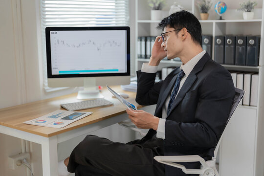 Asian Businessman or Stock Trader Analyzing Financial Market Charts on Computer Monitor in Office