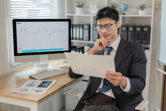 Asian Businessman or Stock Trader Analyzing Financial Market Charts on Computer Monitor in Office