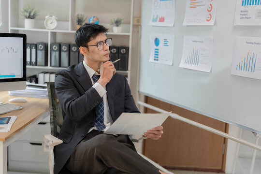 Asian Businessman Presenting Financial Data Charts on Whiteboard in Office Meeting
