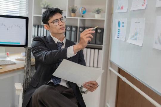 Asian Businessman Presenting Financial Data Charts on Whiteboard in Office Meeting
