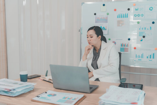 Asian Businesswoman Working on Laptop and Taking Notes at Desk in Office