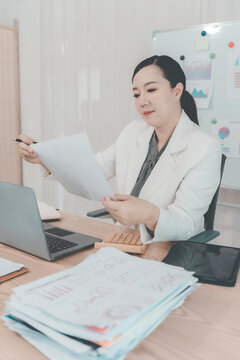 Asian Businesswoman Working on Laptop and Taking Notes at Desk in Office