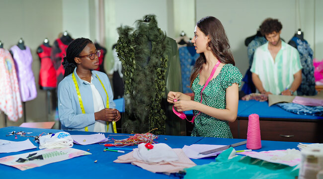 Indian young adult gen z two female wear tape around neck check dummy cloth make dress. Teen tailor girl pair talk speak share idea do paper work learn new course craft skill day at class room place