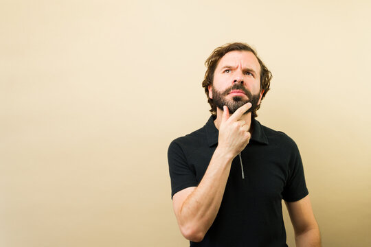Bearded man in a black shirt, pondering a complex idea, looking up with doubt and curiosity
