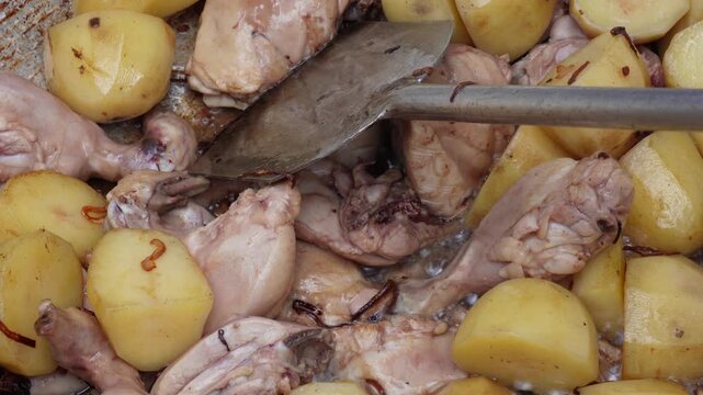 Cooked chicken and potatoes being stirred in a pan
