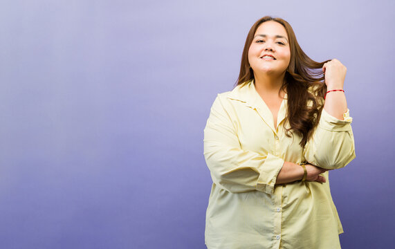 Beautiful confident young woman smiling, pulling hair, expressing body positivity and self-acceptance on purple background