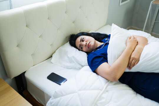 Woman waiting for the phone to ring while trying to sleep on her bed