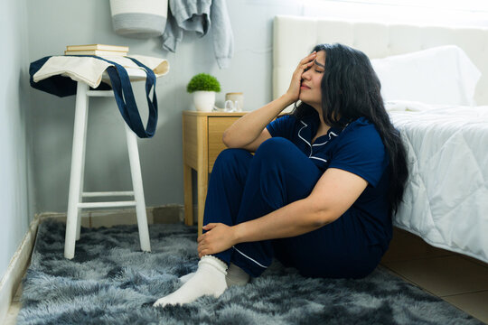 Woman experiencing sadness and emotional distress, feeling upset and lonely while sitting on bedroom floor