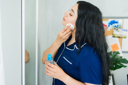 Beautiful woman removing makeup with cotton pad and cleansing water, following her daily beauty routine at home