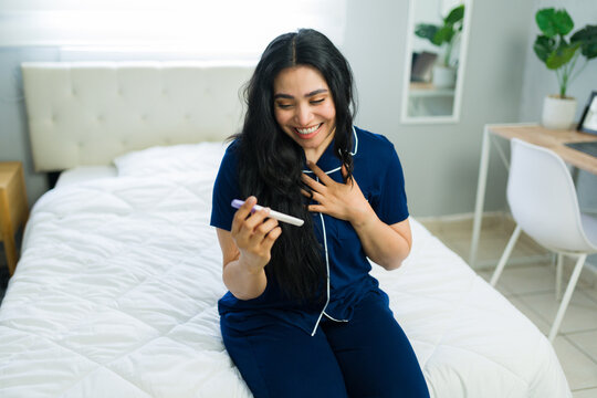 Excited woman receiving positive pregnancy test result, experiencing surprise in her bedroom