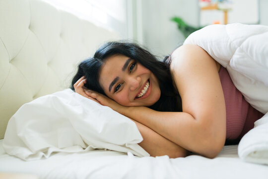 Cheerful young woman waking up in bed, smiling and enjoying a relaxing morning in her comfortable bedroom