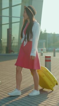 Woman exploring cityscape with luggage, Stylish traveler strolling in sunlight with luggage on lively urban plaza