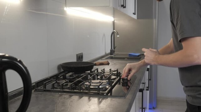Adult man in modern home kitchen holding slotted spatula with visible utensil blur while standing at countertop beside gas cooktop, with kitchen, cooktop, stove, pan detail, showing castiron, grate