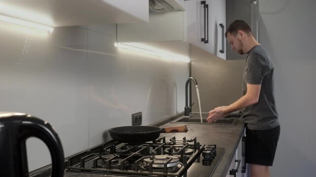 Adult man in modern home kitchen holding slotted spatula with visible utensil blur while standing at countertop beside gas cooktop, with kitchen, cooktop, stove, pan detail, showing castiron, grate
