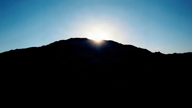 Dawn light breaking over a mountain silhouette against a deep blue sky.