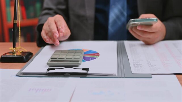 Accountant conducts financial analysis inside corporate office, reviewing investment data, performing audit analysis beside desktop calculator inside investment research analysis.