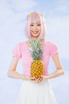 Smiling young woman with pink hair holding pineapple on pastel background