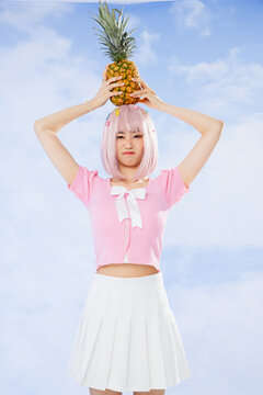 Playful young woman with pink hair balancing pineapple on head