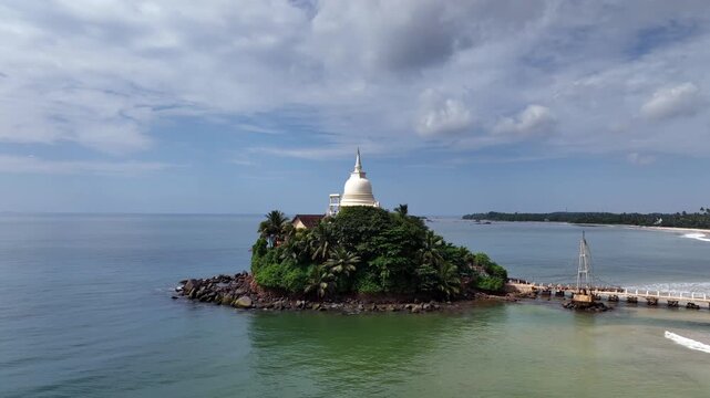 Drone aerial of Parewi Duwa Temple in Matara, Sri Lanka, connected by a scenic footbridge above the Indian Ocean and surrounded by tropical coastal views.