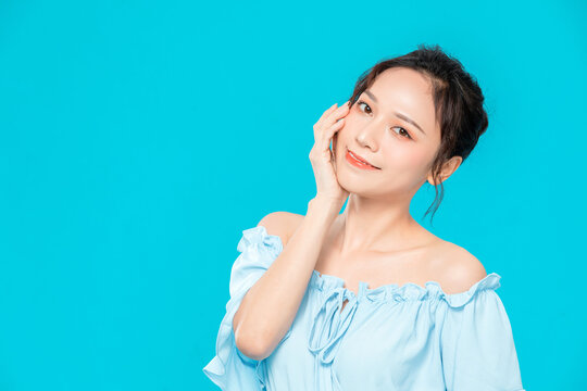 Smiling young woman in light blue off-shoulder blouse posing against turquoise background