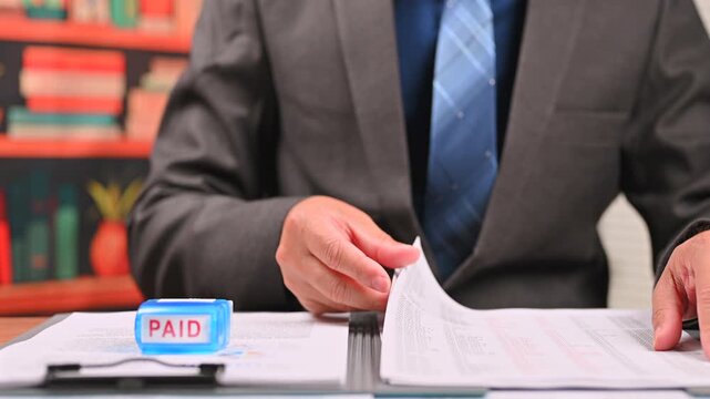 Accountant performing finance audit reviews finance document papers, managing corporate finance audit workflow when reviewing document records marked paid stamp.