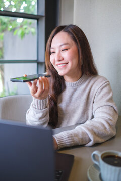 Vertical of a woman holding smart phone and using voice messaging, talking with ai assistant for Artificial intelligence concept while working on laptop