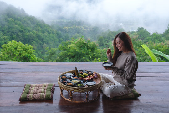 A woman eating breakfast on Northern Thai traditional dining table while looking at foggy mountain views