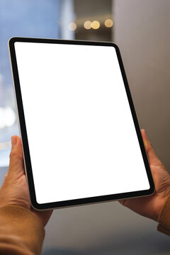 Vertical mockup image of a woman holding digital tablet with blank white desktop screen in cafe