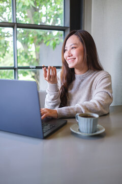Vertical of a woman holding smart phone and using voice messaging, talking with ai assistant for Artificial intelligence concept while working on laptop