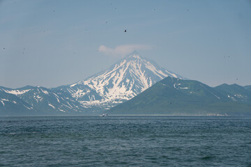 Fototapeta premium Snow-covered Vilyuchinsky Volcano rises above Pacific Ocean in Avacha Bay, Kamchatka, Russia, under clear blue sky. Volcanic landscape, wilderness, nature travel, adventure