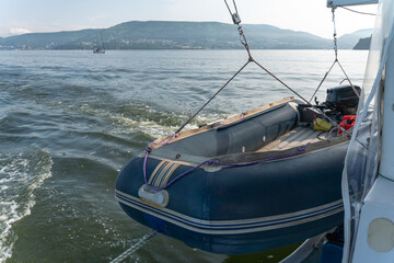 Inflatable motorboat with outboard engine hangs beside moving catamaran with Kamchatka coast in background. Marine transport, boating equipment, navigation, travel, adventure © Sofia