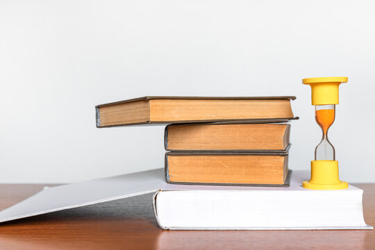 Old books and a yellow hourglass symbolize a deadline and time management concept, with ample copy space for education, learning, knowledge, and business themes.