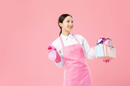 Smiling housekeeper with cleaning supplies on pink background