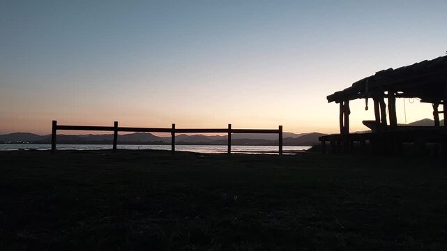 Sunset over Ibiraquera lagoon with grassy shore and rustic shelter