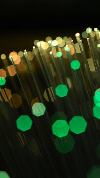 Vertical macro background of glowing fiber optic cables with green and gold bokeh for smartphone wallpaper.
