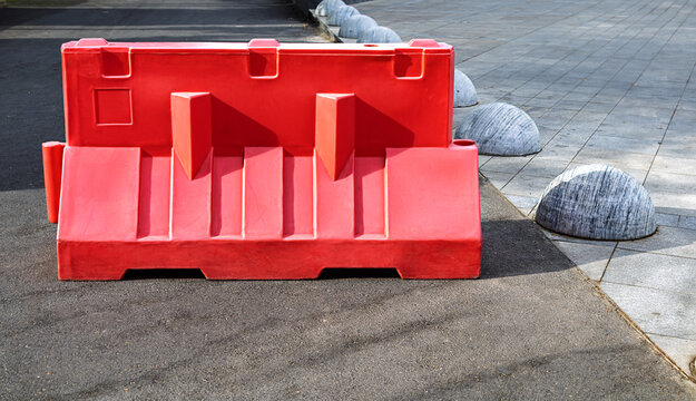 Bright red temporary traffic barrier positioned on an urban street for traffic control and road safety. Clear infrastructure image suitable for road construction, maintenance, restricted access