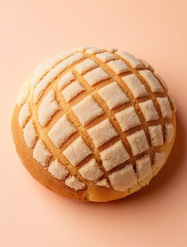 Golden brown concha bread with granulated sugar topping sits on soft peach background. Macro shot shows sweet pastry texture perfect for bakery or breakfast ads.