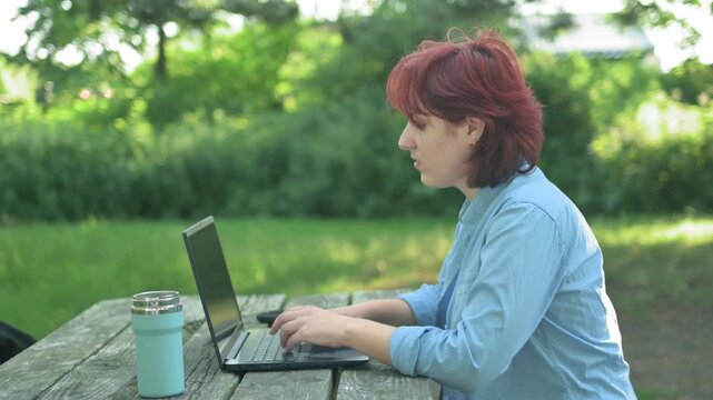Red-haired girl closing her laptop after an online exam or study session in a public park. Concept of finished education or work.