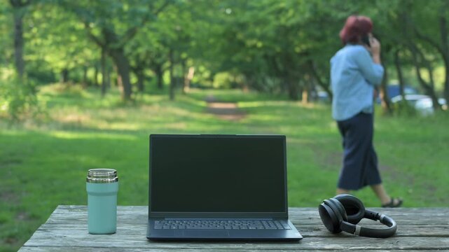 Open laptop on table with blurry redhead woman talking on phone in background.