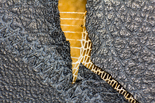 Close up of damaged black synthetic leather upholstery showing interior mesh material and torn texture
