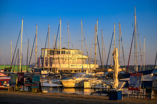 Pula, Croatia - August 04, 2026: Yachts in the port of Pula. A serene seaside town bathes in the golden light of sunset, with anchored boats gently rocking in the calm harbor waters, and diverse archi