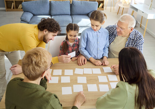 Family children grandparents parents learning memory boardgame. They play a card game at a table, with girls building focus and strategy. Strong family bonding and playful education.