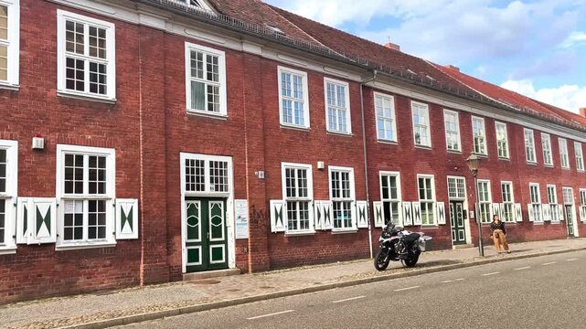 Dutch Quarter, Red brick building with green doors and white shutters, motorcycle parked on the street, pedestrians walking by, showcasing urban architecture in a European city