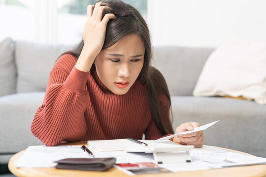 Business financial concept, stressed asian young woman hand checking list with bill for calculate accounting expense credit card payment on due deadline, trying to find money to pay debt on table.