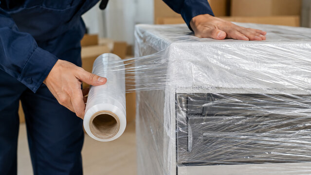 A person wrapping a piece of furniture with clear plastic stretch film for protection during moving or storage.
