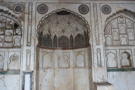 Ancient Islamic architecture with ornate stone carvings, weathered marble mihrab wall, traditional Mughal style arched alcoves
