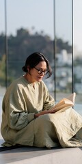 Naklejka premium Woman reading a book on a modern glass terrace in sunlight for relaxation background and mindful home lifestyle imagery