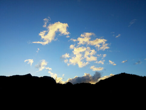 Scattered Sunlit Clouds Above A Dark Mountain Ridge