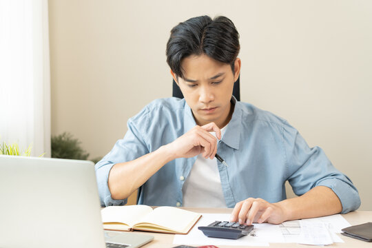 Saving money wealth concept, asian young business man, male using calculator for calculate saving cost, cash finance planning to spend enough money on his income for save money, payment tax, investing